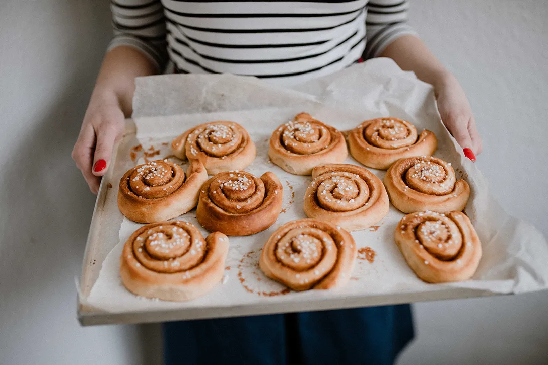Teller mit drei frisch gebackenen schwedischen Zimtschnecken (Kanelbullar) mit Hagelzucker, bereit zum Genießen.