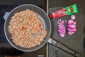 Tomatenmark und gewürfelter Knoblauch werden zum angebratenen Hackfleisch in der Pfanne gegeben und mitgebraten