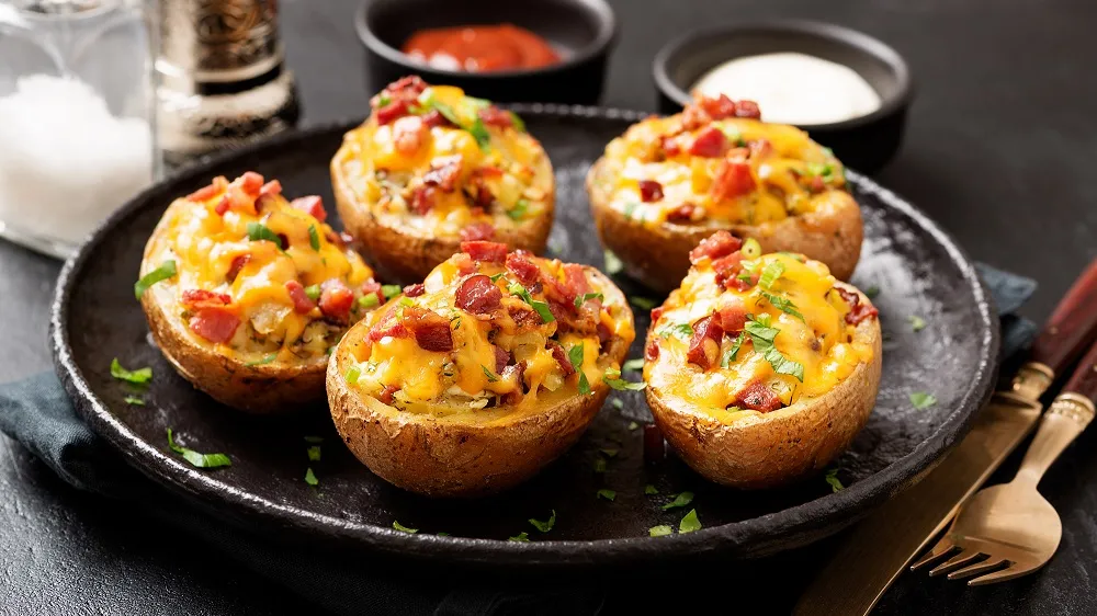 Vier gefüllte Ofenkartoffeln mit geschmolzenem Cheddar, knusprigem Bacon und frischen Kräutern