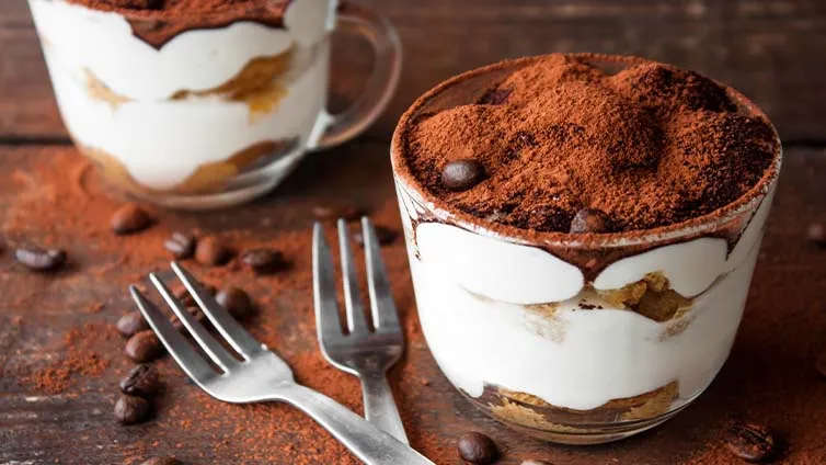 Vier Gläser Tiramisu, geschichtet mit Löffelbiskuits, Creme und Kakaopulver
