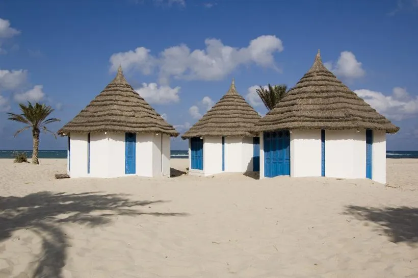 Weiße Hütten an einem Strand auf Djerba mit dem Meer im Hintergrund, einladend für einen entspannten Urlaub in Tunesien.