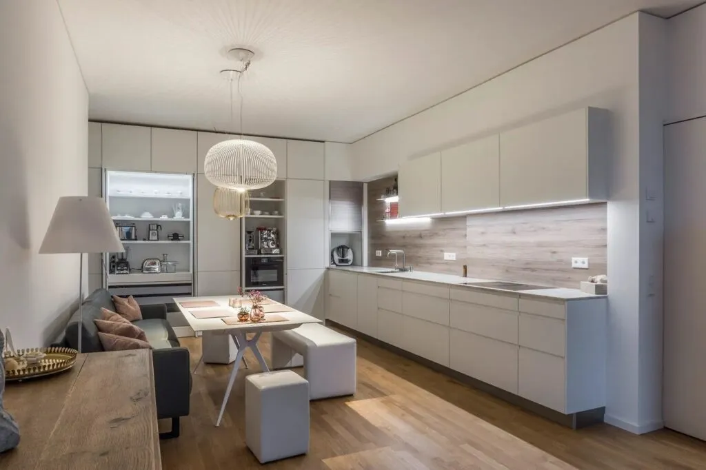 Weiße, moderne Küche in U-Form mit einer Essecke mit Sofa auf der linken Seite und einem Rollladenschrank auf der rechten Seite.