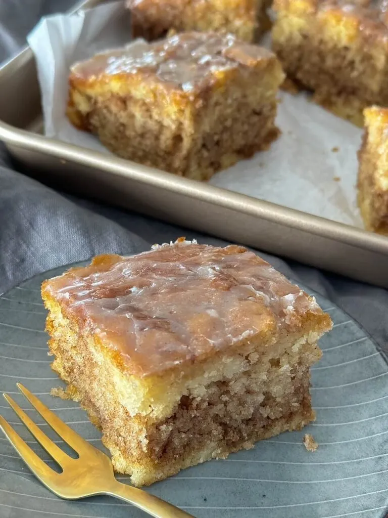 Zimtschnecken Kuchen wird mit glänzender Vanilleglasur bestrichen, ein perfekter Blechkuchen für schnelle Genießer