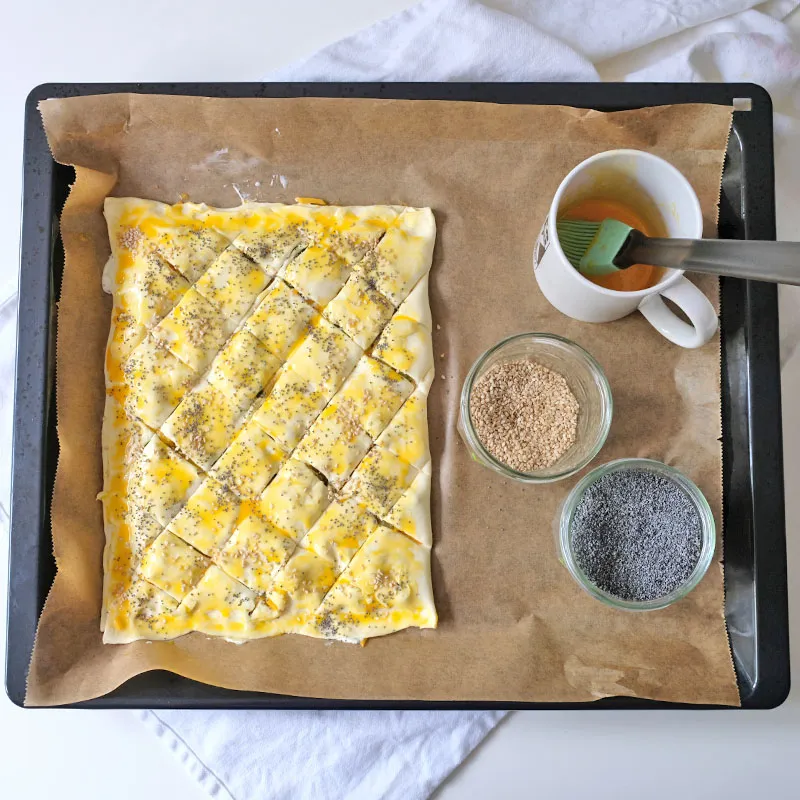 Zubereitungsschritt: Blätterteig mit Eigelb bepinselt und mit Sesam und Mohn bestreut