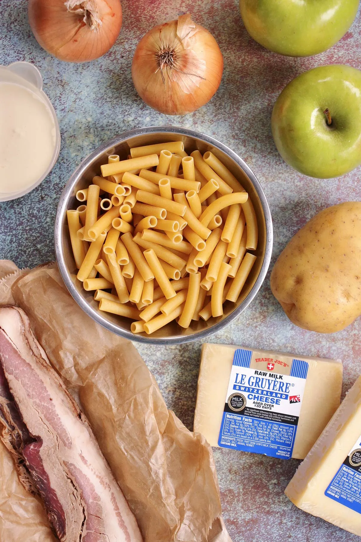 Zutaten für Älplermagronen, darunter Röhrennudeln, Käse, Kartoffeln, Zwiebeln, Äpfel und Speck