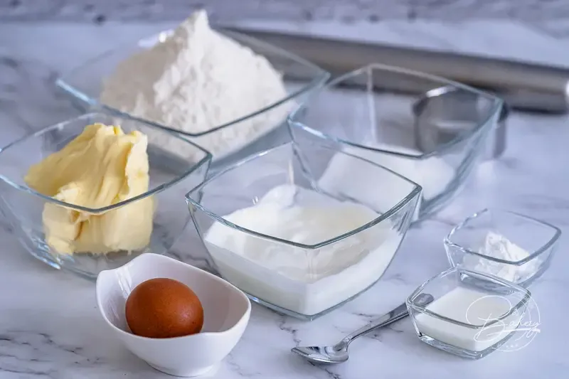 Zutaten für Scones: Mehl, Zucker, Backpulver, Salz, Margarine und griechischer Joghurt auf einem Holztisch