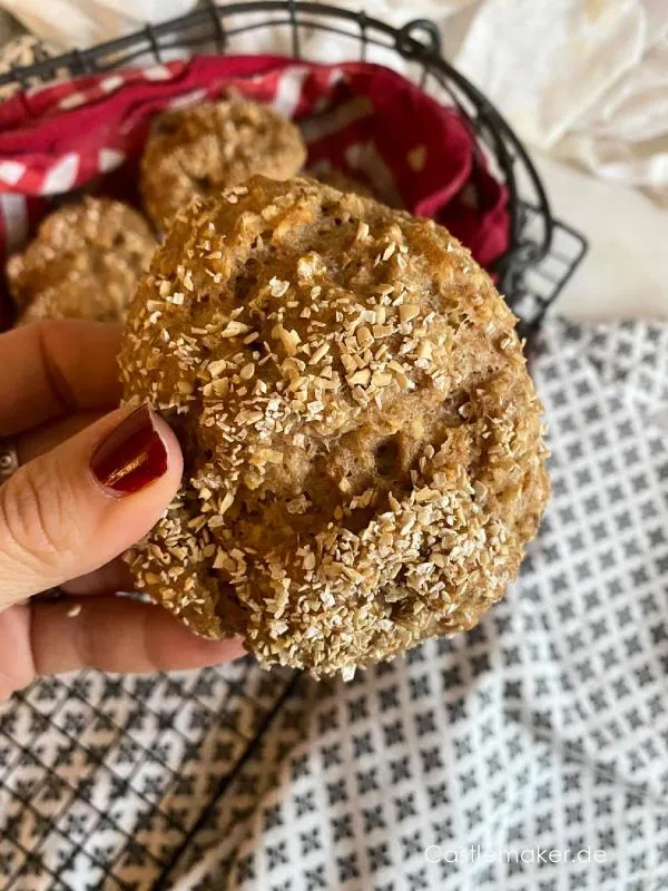 Zwei frisch gebackene Dinkel-Hafer-Quarkbrötchen, eines halbiert, auf einem Teller
