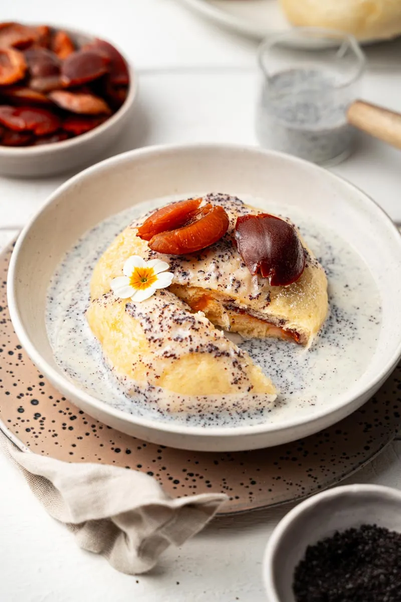 Zwei Germknödel mit Pflaumenfüllung und cremiger Mohn-Vanille-Soße auf einem Teller angerichtet
