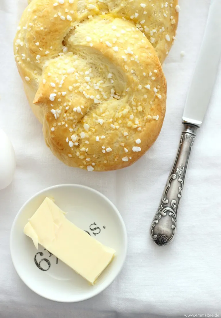 Zwei ungebackene Hefezöpfe, liebevoll geflochten und bereit zum Bestreichen, auf Backpapier liegend