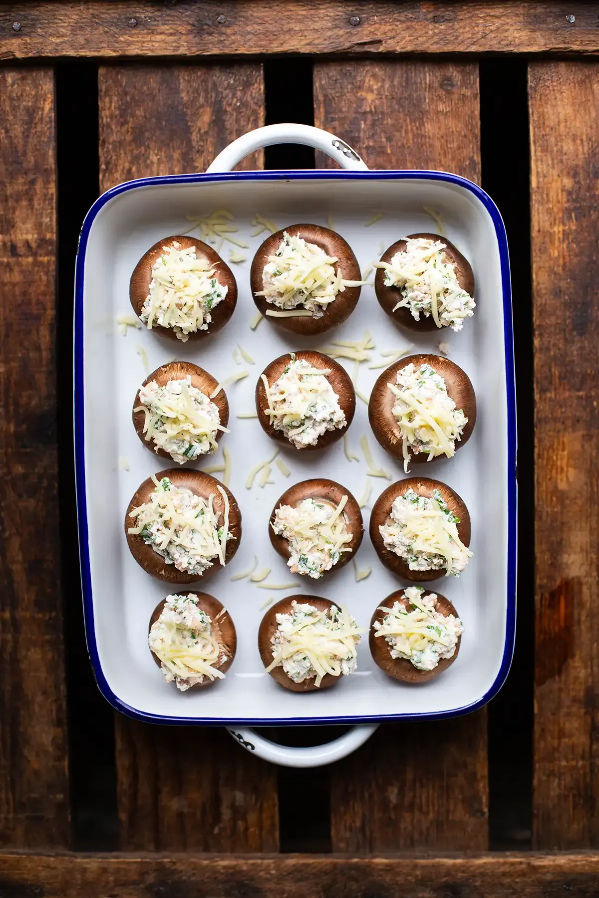 Zwölf ungekochte gefüllte Champignons in einer blauen Auflaufform, bereit zum Backen oder Grillen