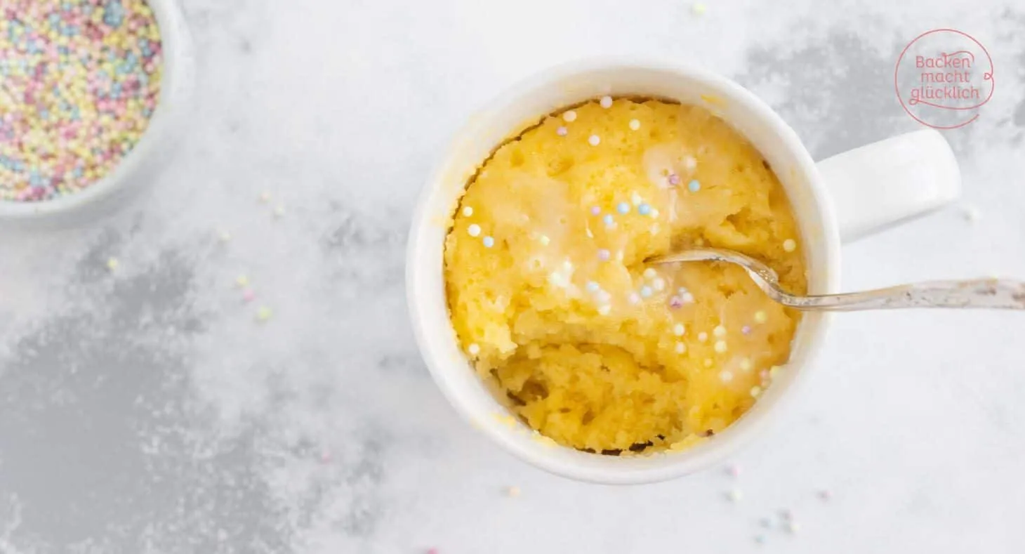 Eine Tasse mit einem fertigen Mug Cake, garniert mit Puderzucker und Streuseln
