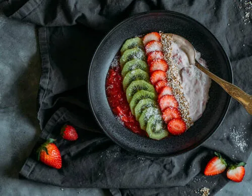 Frühstücksbowl mit Erdbeeren und Rhabarber in Schüssel vor dunklem Hintergrund.