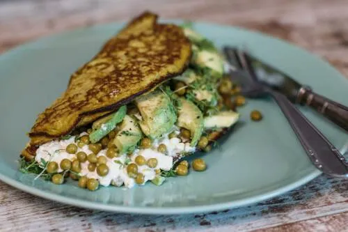 Grünes Frühstücksomelett auf Teller mit Besteck vor dunklem Hintergrund.