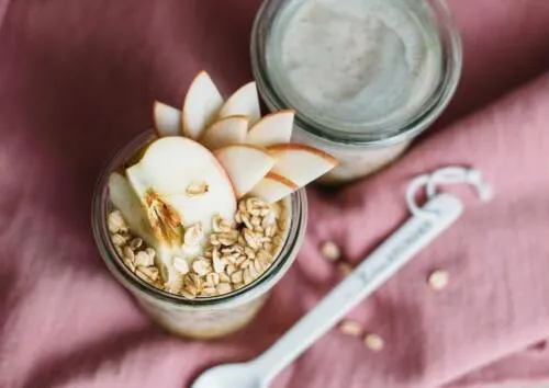 Selbst gemachte Bircher-Overnight-Oats in einem Glas mit Apfelscheiben garniert.