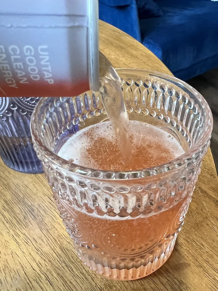 Ein hellrosa Kin Spritz wird in ein strukturiertes Glas auf Holz gegossen.