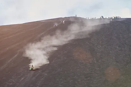 Ein Sportler beim Volcano Boarding rast einen Vulkanhang hinunter
