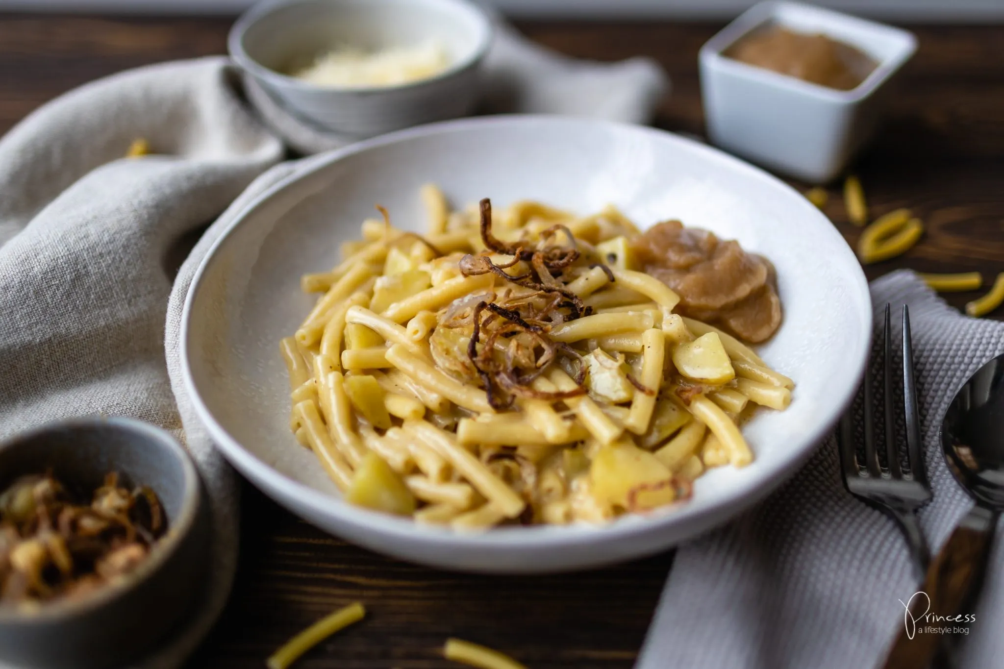 Ein Teller Älplermagronen, garniert mit Röstzwiebeln und einer Schüssel Apfelmus