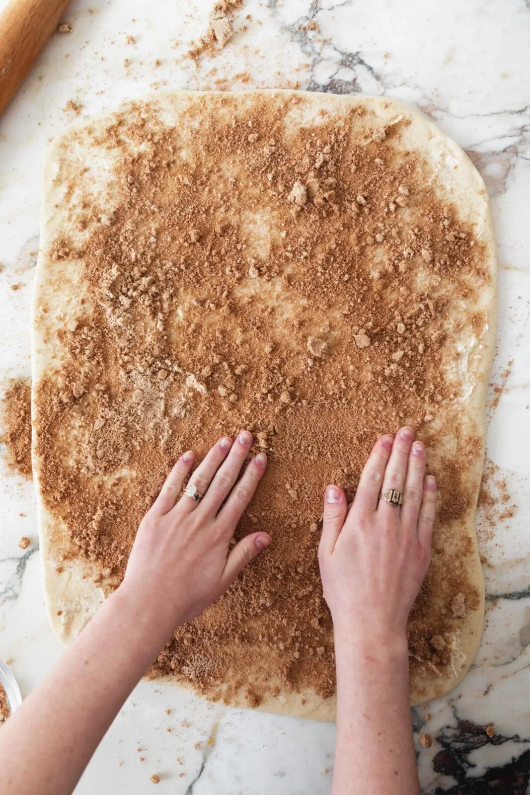 Eine große rechteckige Platte Zimtschnecken-Teig, die mit der Zimtfüllung bestrichen wird