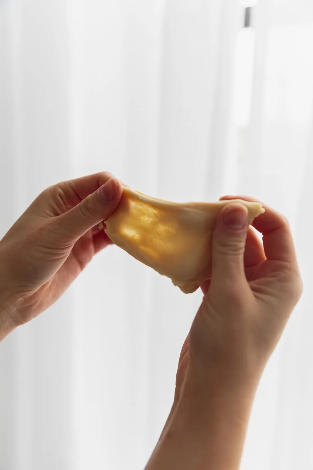 Eine Hand hält ein dünnes Stück Teig gegen das Licht, um den Fenstertest zu demonstrieren