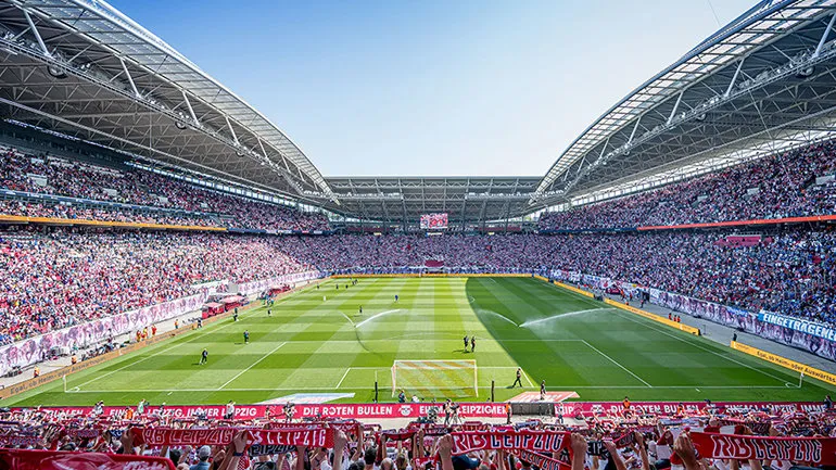 Eine Nahaufnahme von Fußballspielern, die auf dem Feld um den Ball kämpfen, mit dem Logo von RB Leipzig im Hintergrund.