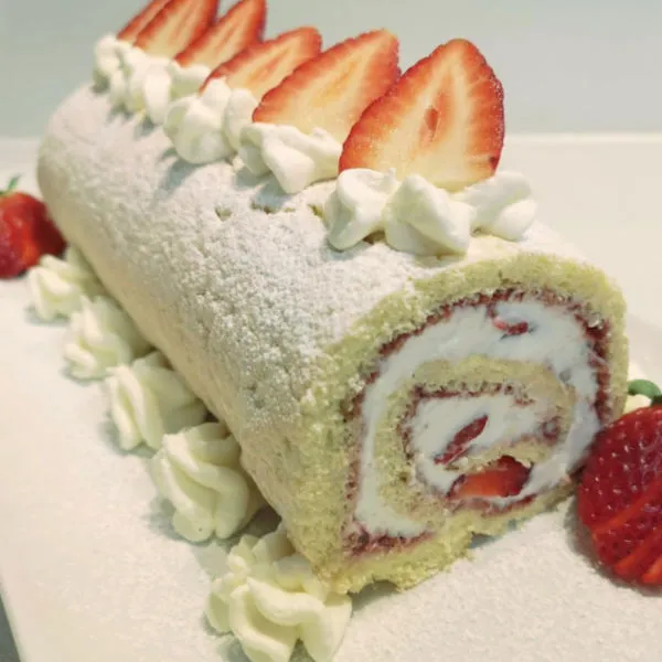 Fertige Erdbeer-Biskuitrolle, gefüllt mit Sahne und frischen Erdbeeren, dekoriert