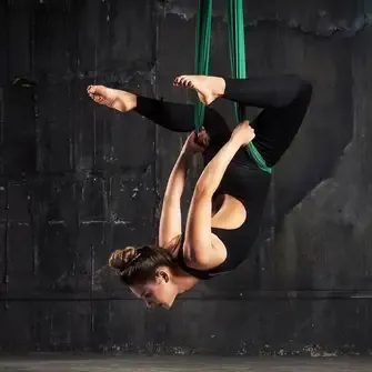 Frau haengt kopfueber in gruenem aerial yoga tuch und fuehrt eine akrobatische uebung in einem dunklen studio aus