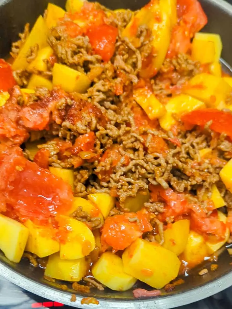 Gewürfelte Kartoffeln und Tomaten werden in den Eintopf gegeben