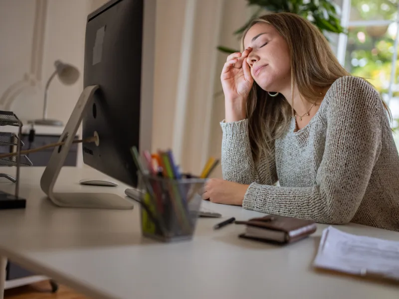 Junge Frau sitzt müde im Homeoffice am Schreibtisch.