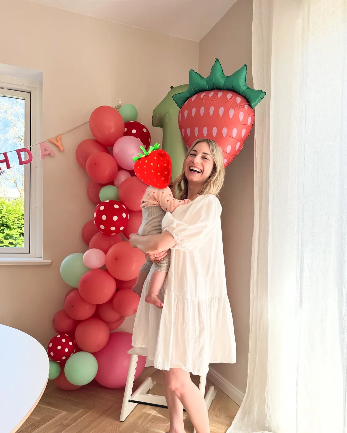 Lynn lächelt mit ihrem Baby in den Armen, das Baby isst Kuchen