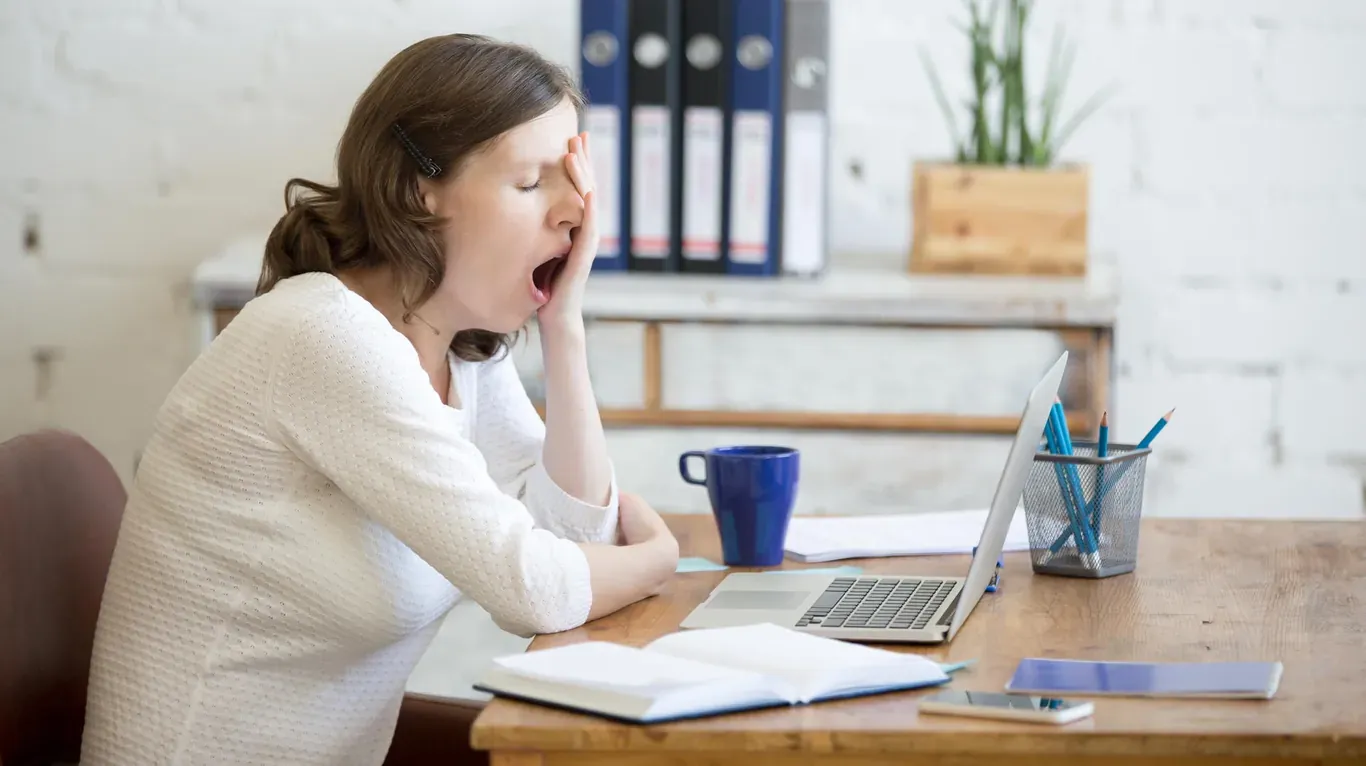 Müde Frau am Schreibtisch, die unter Energiemangel leidet