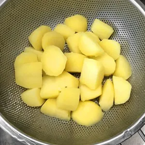 Vorgekochte Kartoffelstücke dampfen in einem Sieb aus