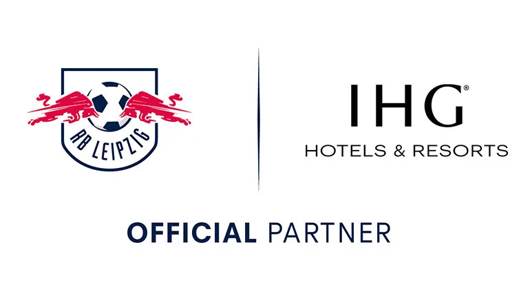 Zwei Personen in RB Leipzig-Trikots stehen lächelnd in einem modernen Hotel-Foyer.