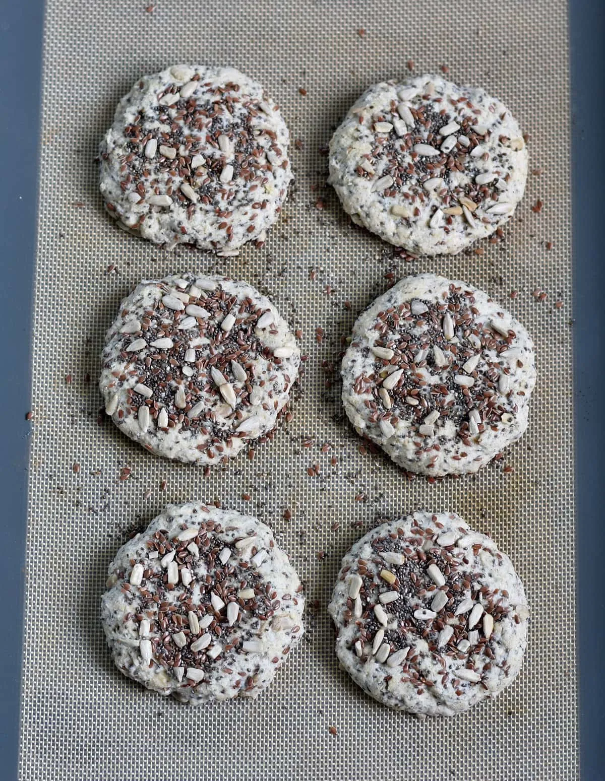 6 glutenfreie Brötchen mit Körnern auf Backunterlage vor dem Backen