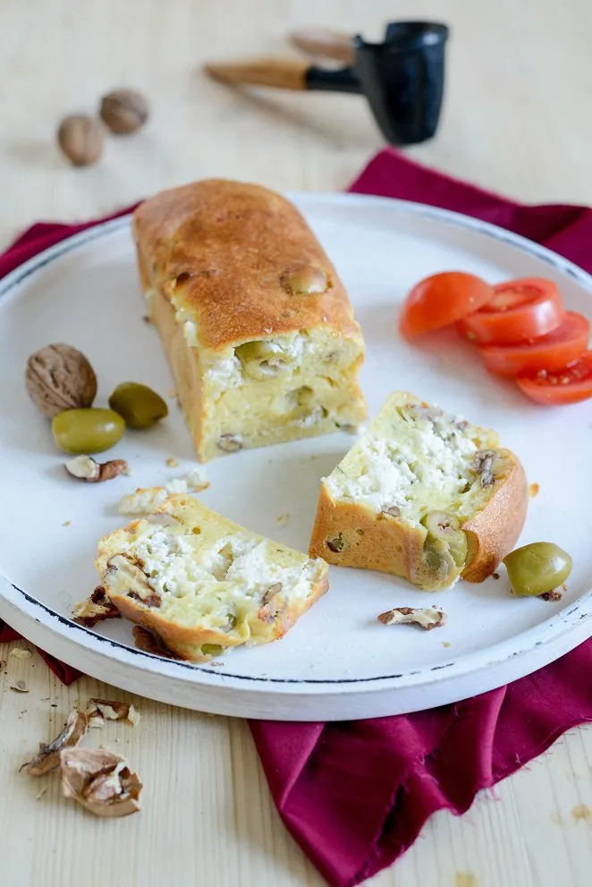 Anschnitt eines herzhaften Kuchens mit Oliven und Ziegenkäse auf einem Holzbrett