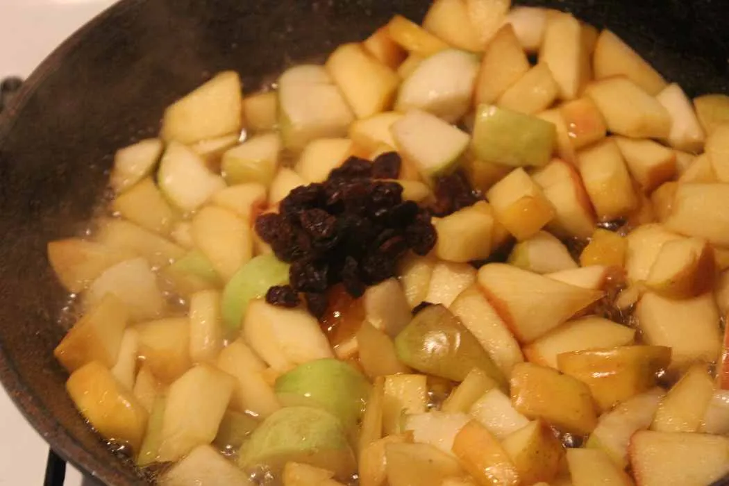 Apfelstücke, Rosinen und Amaretto werden in der Pfanne vermischt