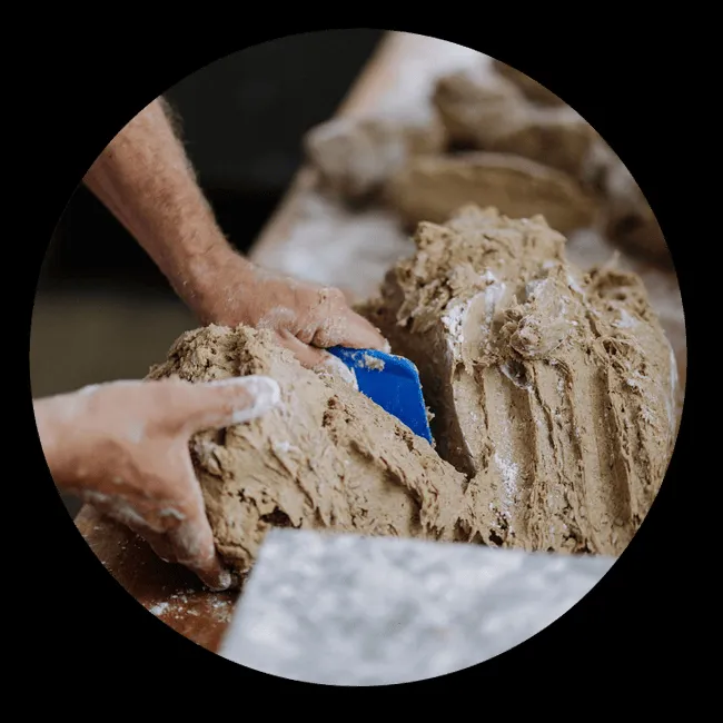 Bäckerhände beim Portionieren von Teig auf einer bemehlten Arbeitsfläche.