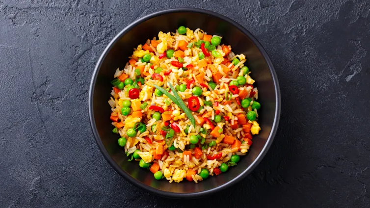 Bunte Gemüse-Reispfanne in einer Schüssel, mit frischen Kräutern garniert.