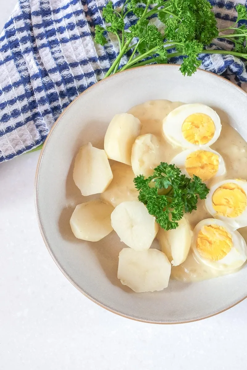 Eier in cremiger Senfsoße in einer Schale, daneben gekochte Kartoffeln