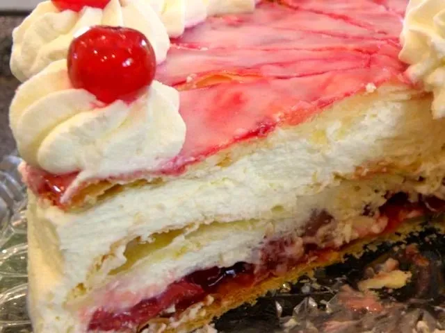 Ein angeschnittenes Stück Holländer Sahnetorte, das die Schichten und die Füllung zeigt