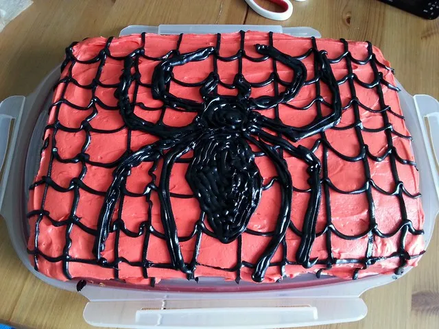 Ein fertig dekorierter Spider-Man Erdbeerkuchen mit rotem Frosting und schwarzem Spinnennetz-Design