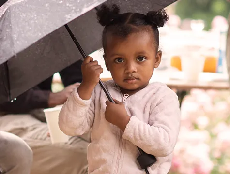 Ein kleines Kind steht mit Regenschirm im Regen.