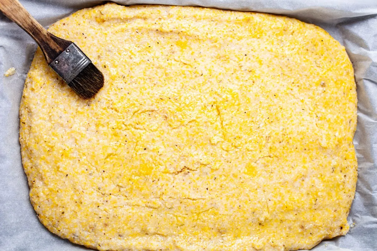 Ein Küchenpinsel auf einem Polenta-Pizzaboden, der mit Olivenöl bestrichen ist