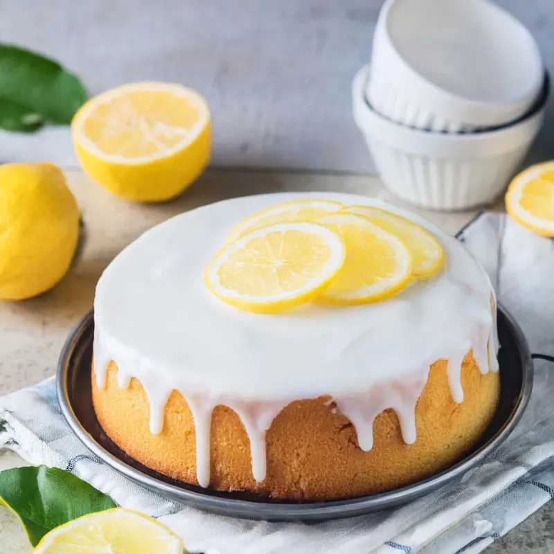 Ein perfekt gebackener, luftiger Zitronenkuchen mit weißer Glasur auf einem Servierteller