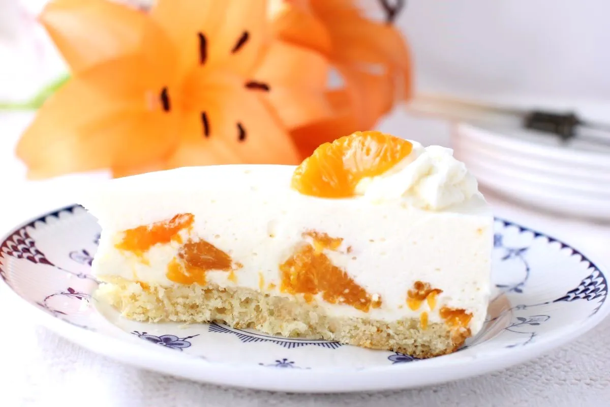 Ein Stück Mandarinen-Sahnetorte mit einer orangefarbenen Lilienblüte im Hintergrund.