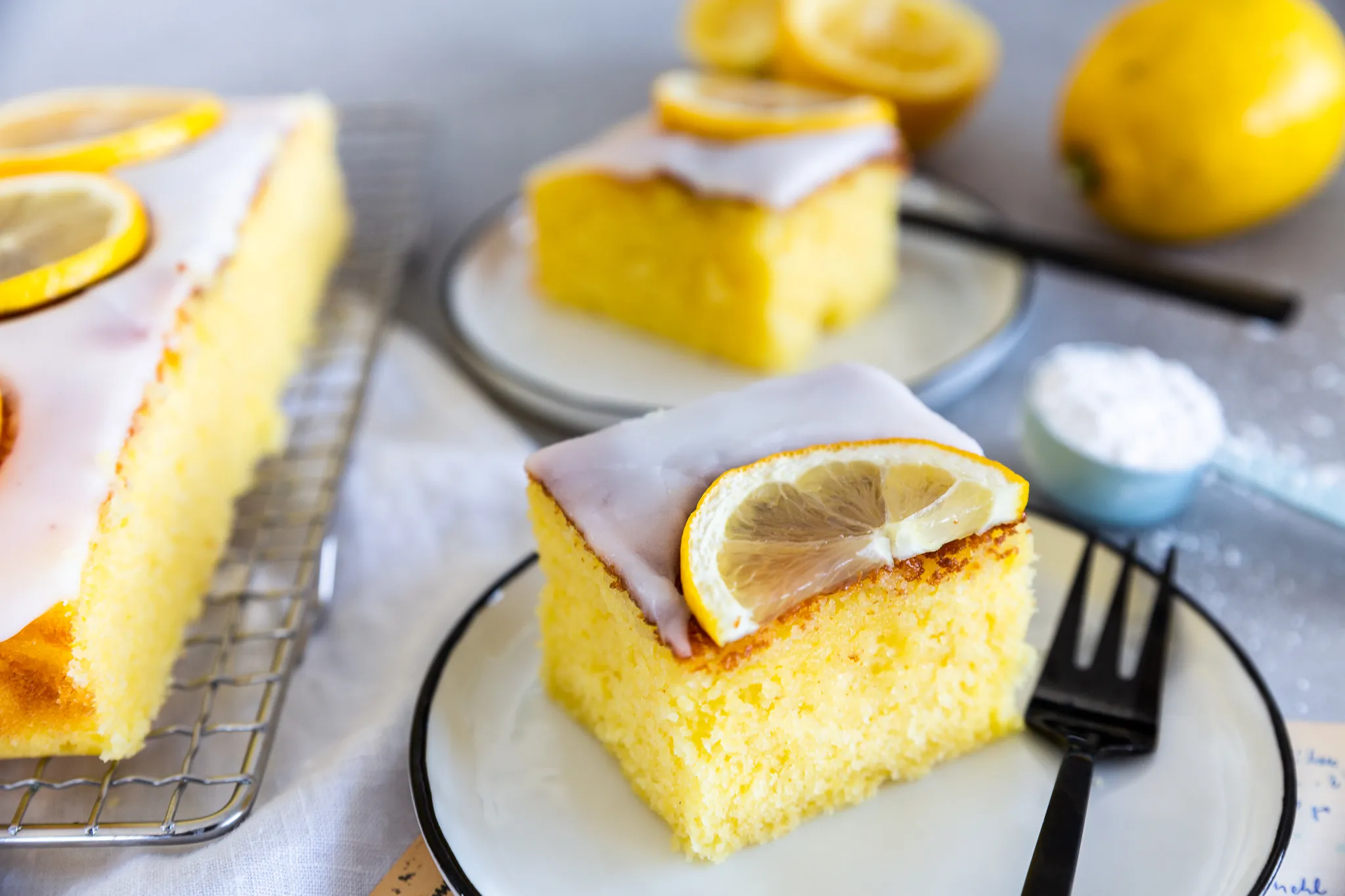 Ein Stück saftiger Zitronenkuchen vom Blech mit frischer Glasur und Zitronenzesten.