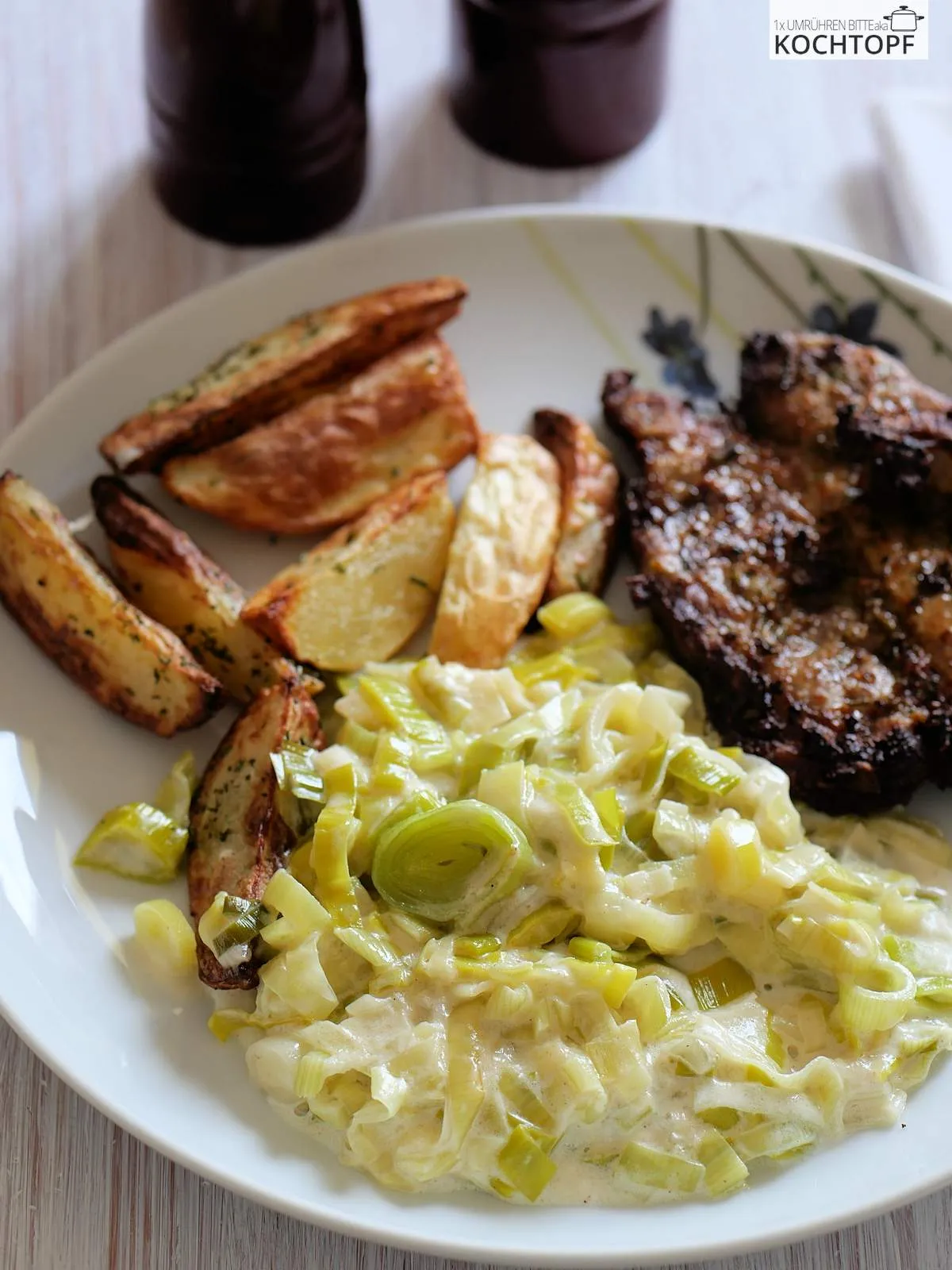 Ein Teller mit cremigem Lauchgemüse, knusprigen Wedges und einem gebratenen Nackensteak
