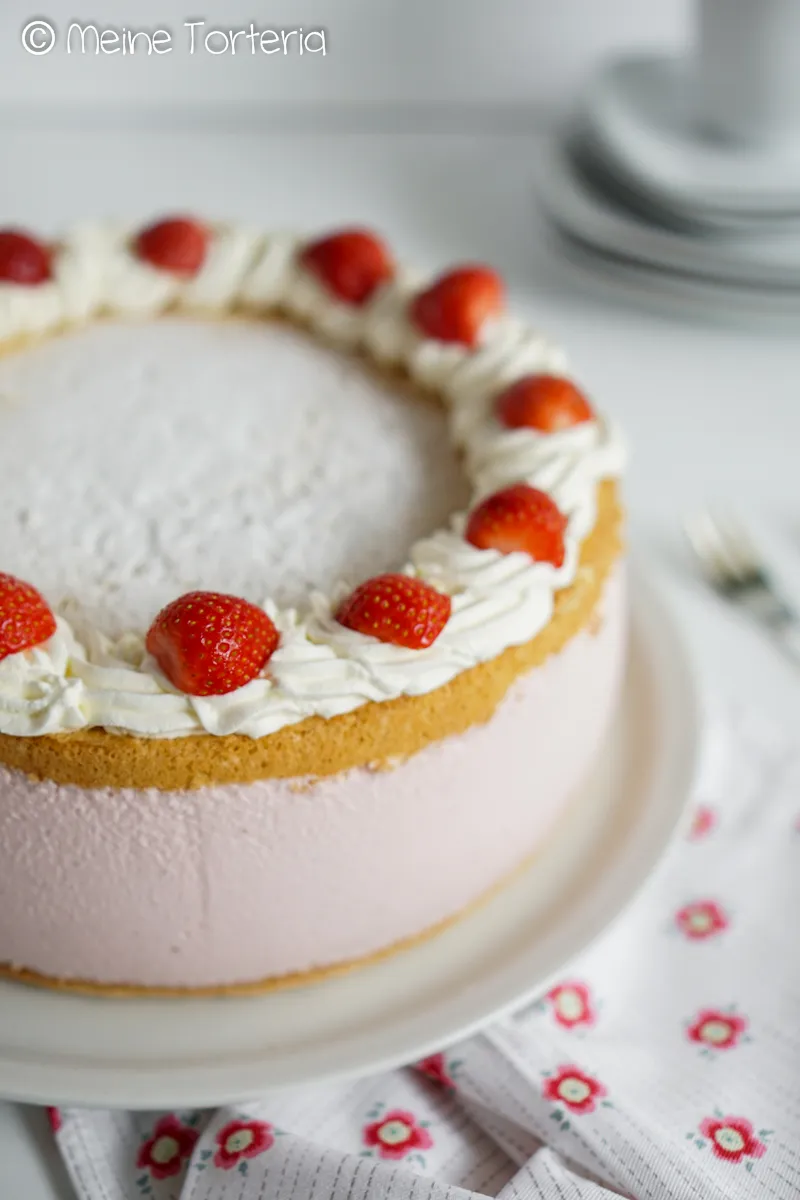 Eine angeschnittene Erdbeer-Käsesahnetorte mit mehreren Schichten und frischen Erdbeeren