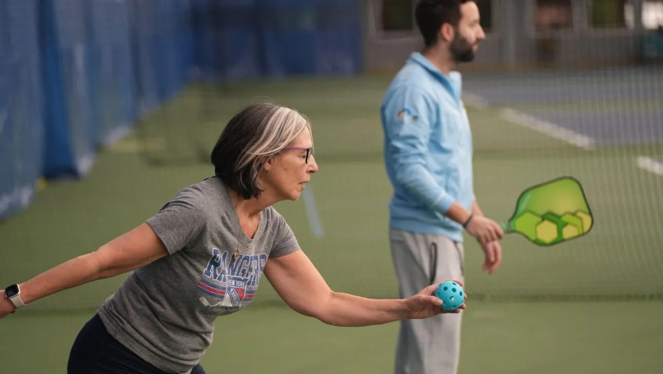 Eine Frau bereitet sich darauf vor, einen Padel-Ball auf einem Indoor-Platz aufzuschlagen, neben einem Mann mit Schläger
