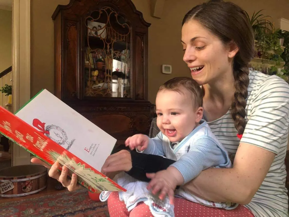 Eine Frau mit kurzem, dunklem Haar liest einem Kleinkind, das auf ihrem Schoß sitzt, ein Buch vor.