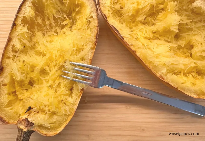 Eine Gabel kratzt das fasrige Fruchtfleisch aus einer gebackenen Spaghettikürbis-Hälfte